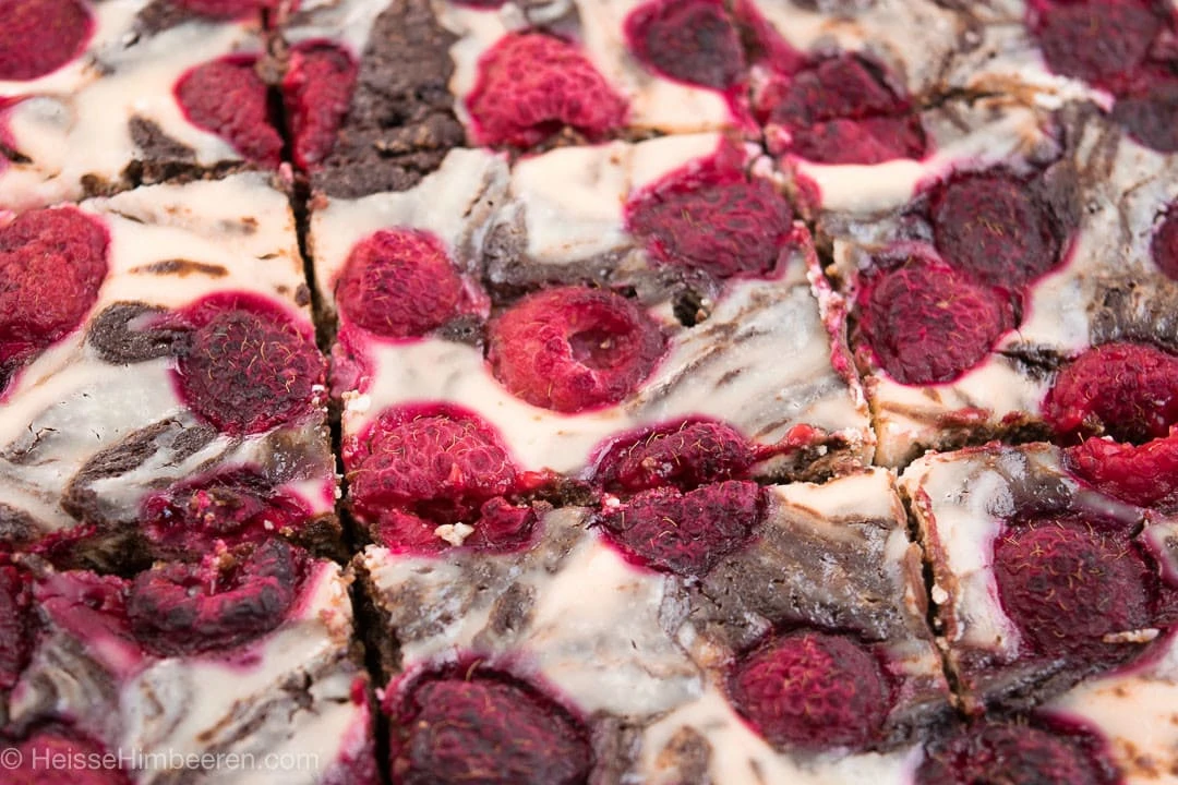 Ein Blech mit geschnittenem Cheesecake Brownies mit Himbeeren.