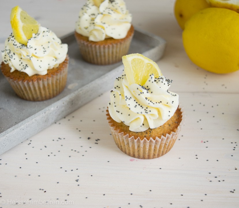 Ein Zitronen Mohn Cupcakes im Fokus. Im Hintergrund sind zwei Zitronen