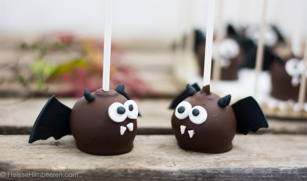 Zwei Fledermaus Cake Pops zu Halloween auf einem Holzbrett als süße Backidee.