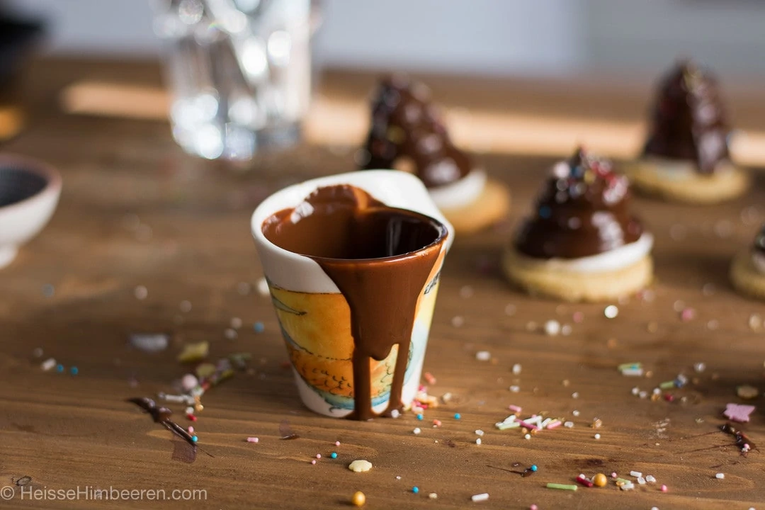 Eine Tasse mit flüssiger Schokolade. Im Hintergrund sind Schokoküsse unscharf zu erkennen