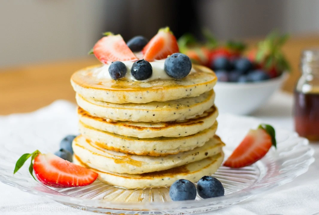 Zitronen Pancakes gestapelt auf einem teller mit Erdbeeren und Blaubeeren und Joghurt