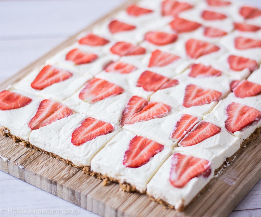 Ein Erdbeer-Cheesecake-Blechkuchen, man sieht die Erdbeeren auf dem Kuchen angeschnitten liegen.