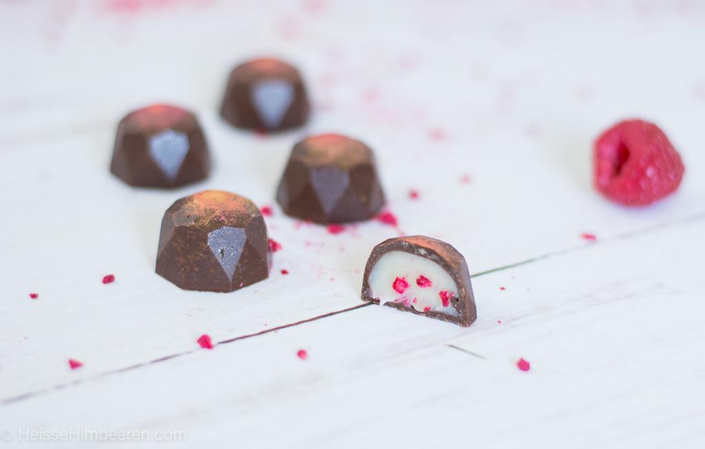 Eine halbe Himbeer Praline die selber gemacht wurde. Man sieht die Füllung die weiß ist mit Himbeerstückchen drinnen.