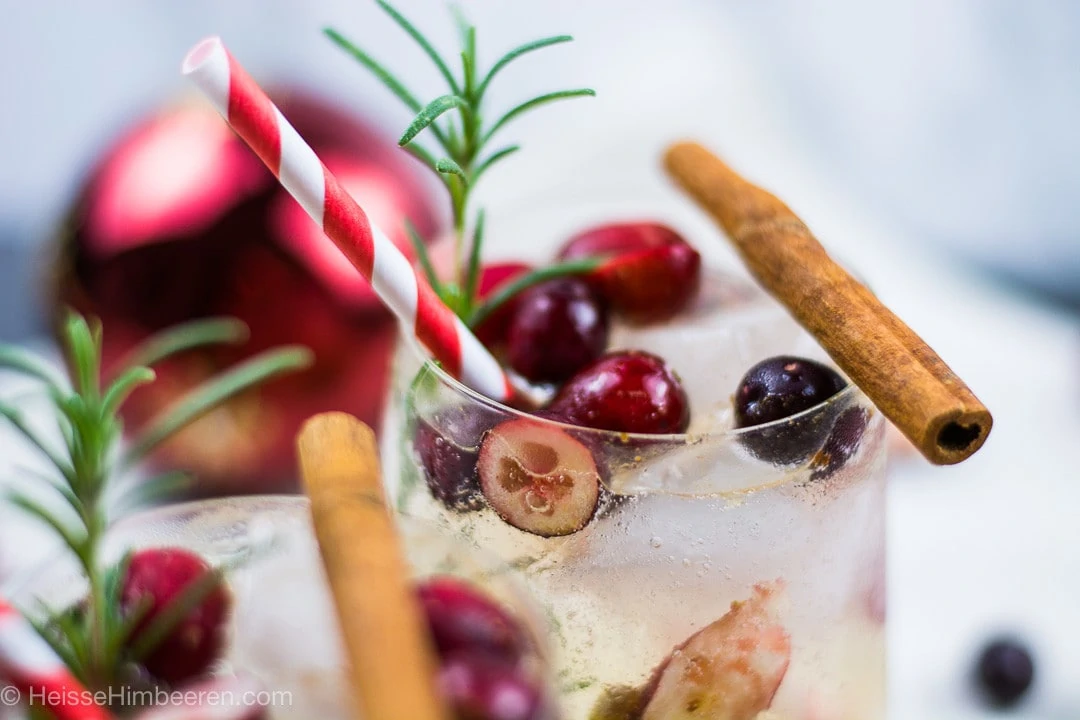 Eine Nahaufname des weihnachtlichen christmas cocktails mit Cranberry, Zimtstange und Rosmarin