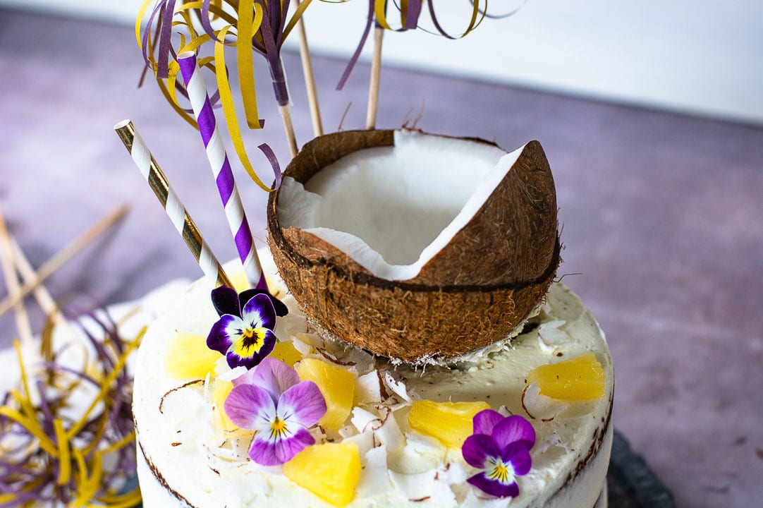 Die Pina Colada Torte von oben. Sie hat eine halbe Kokosnuss, Ananas und Blüttenblätter als Dekoration