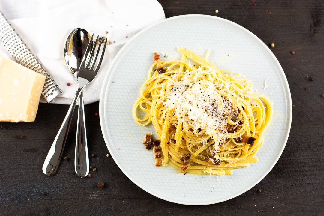Ein weißer Teller mitSpagetti Carbonara. Die Carbonara hat Speckwürfel und Parmesan