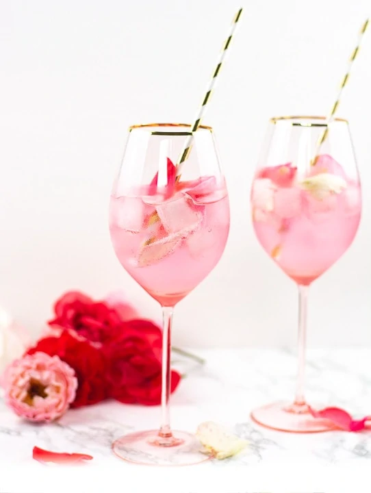 Zwei Gläser Pink Rose Cocktail, im Hintergrund liegen rote Rosen.