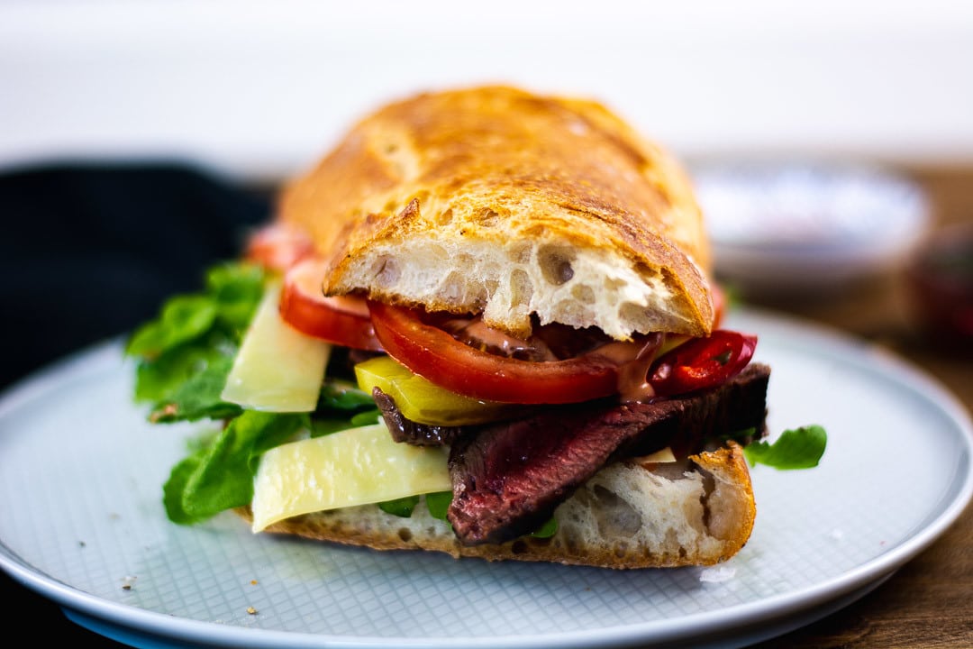 Ein Steak Sandwich aus dem vorne eine Tomate, ein Steak und Parmesan hervorschaut