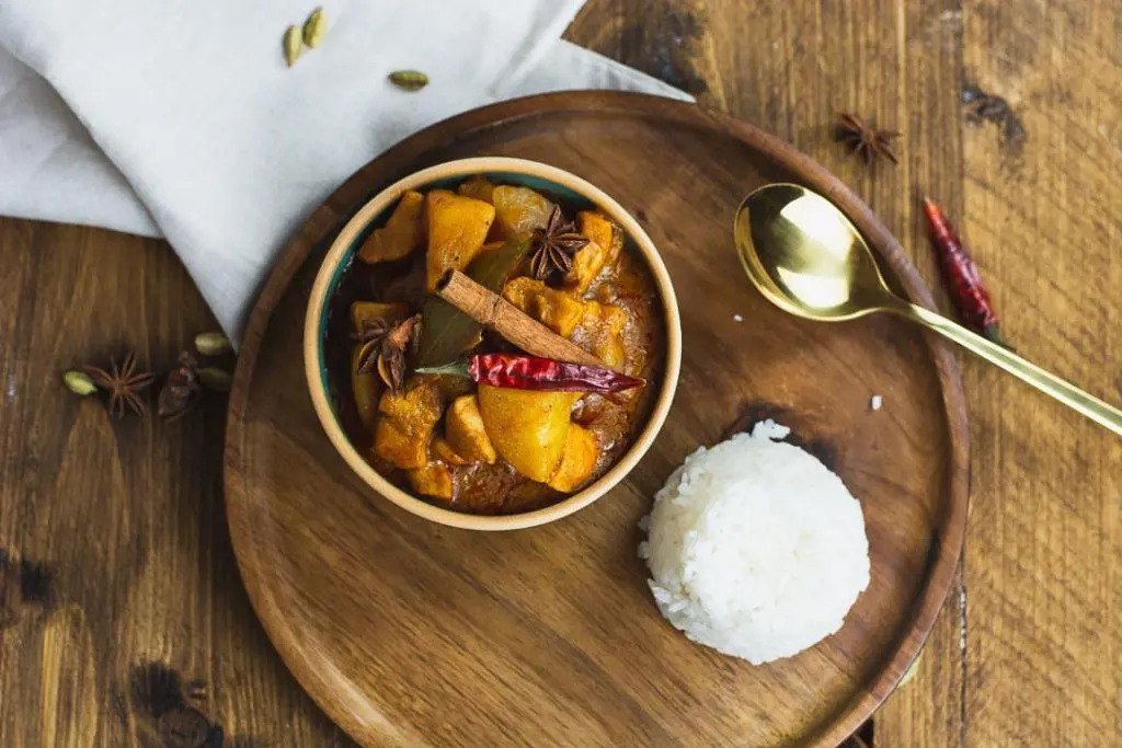 Auf dem Tisch steht das Curry mit einem Löffel und einer Schale Reis.