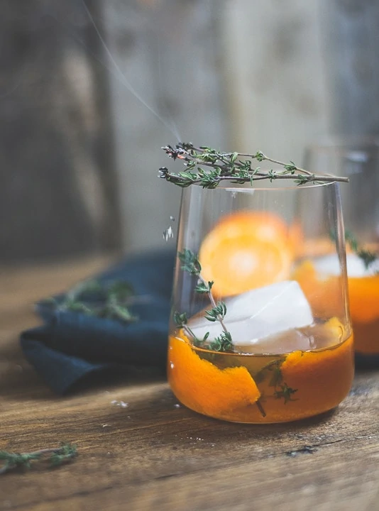 Ein Old Fashioned mit Mandarine und braunem Rum auf einem Holztisch.