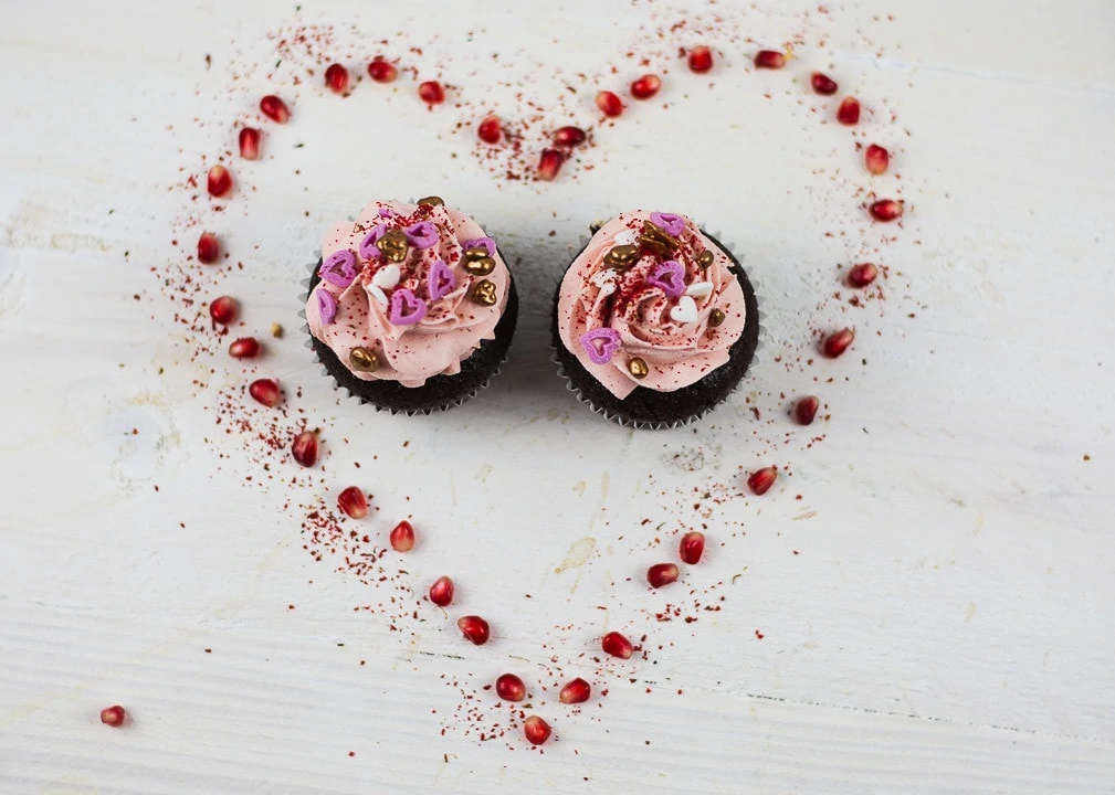 Ein Herz aus Granatäpfel mit zwei Valentinstag Cupcakes