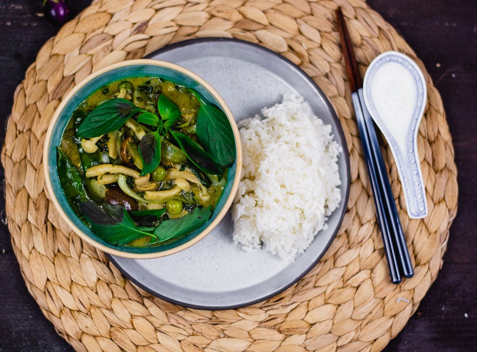 Grünes Thai Curry auf einem Teller. Daneben liegen Stäbchen und ein asiatischer Suppenlöffel