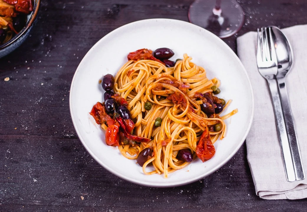 Spaghetti Puttanesca vegetarisch auf einem Teller mit Besteck daneben