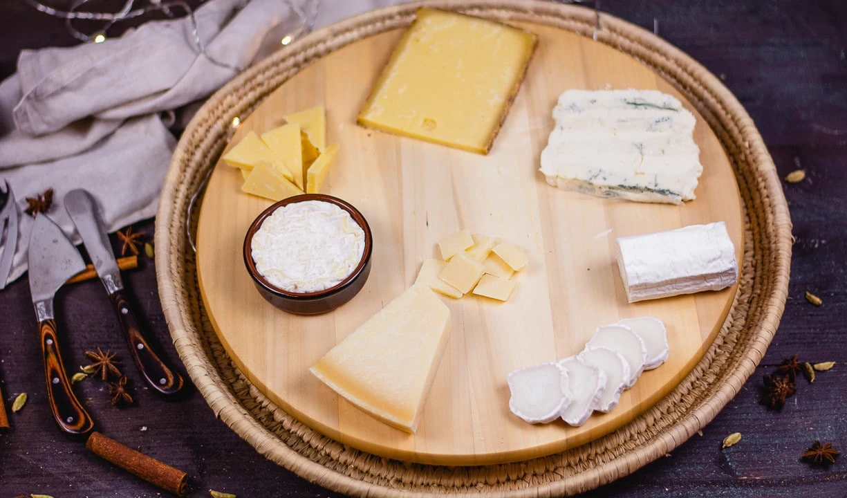 Fünf verschiedene Käse, Bergkäse, Pecorino, Gorgonzola, Ziegenkäserolle und Brie, auf einem runden Holzbrett