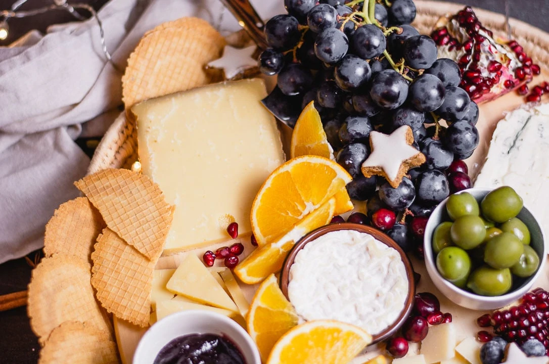 Orangenspalten, Weintrauben, Granatapfel, Oliven und Zimtsterne liegen als Dekoration auf der Käseplatte
