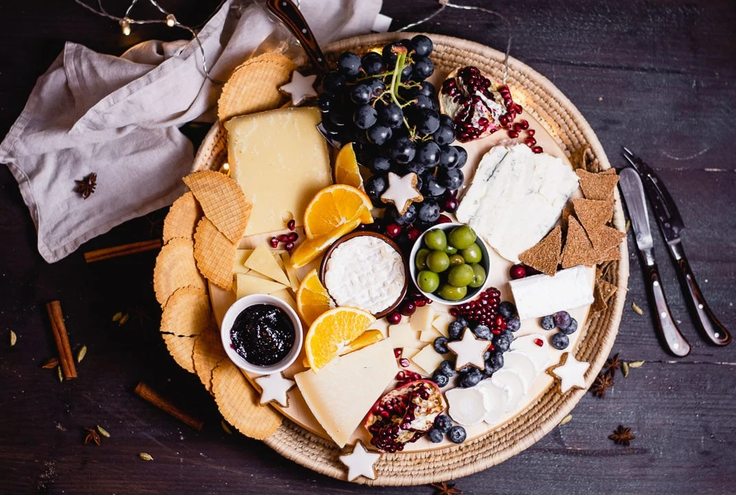 Käseplatte mit Weintrauben, Granatapfel, Oliven, Crackern und Zimststernene von oben fotografiert 