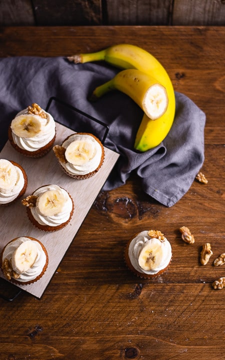 Bananen Cupcakes auf einem braunen Holztisch. Daeben liegen Bananen und Walnüsse als Deko