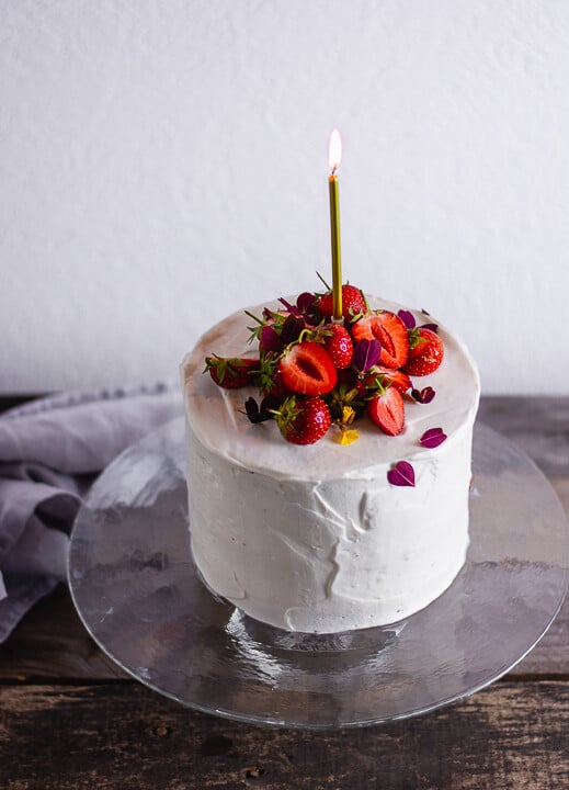 Ein Kuchen in weiß mit Erdbeeren auf dem Kuchen und einer goldenen Kerze die brennt