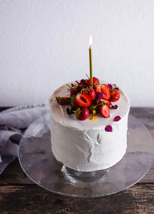 Ein Kuchen in weiß mit Erdbeeren auf dem Kuchen und einer goldenen Kerze die brennt.