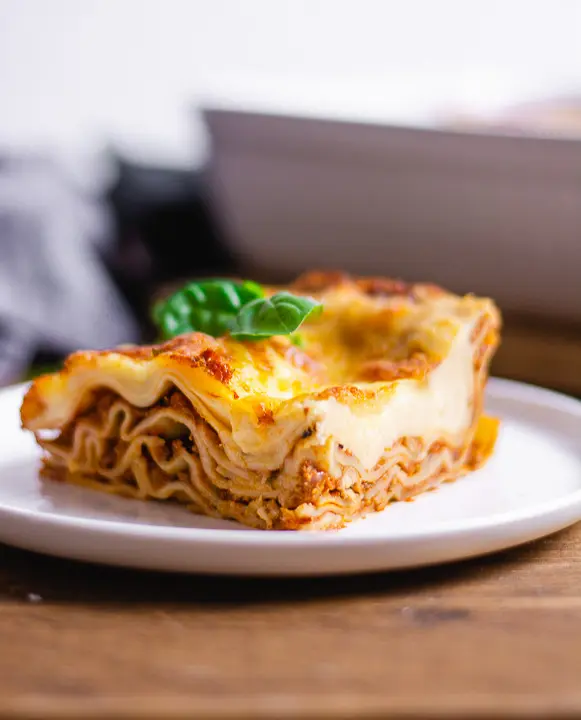 Ein Stück vegetarische Lasagne Bolognese mit Basilikumblatt auf einem Teller.