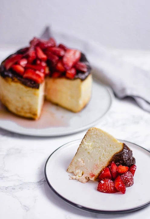 Ein Stück Cheesecake auf einem Teller. Viele Erdbeerstückchen liegen auf dem Kuchen.