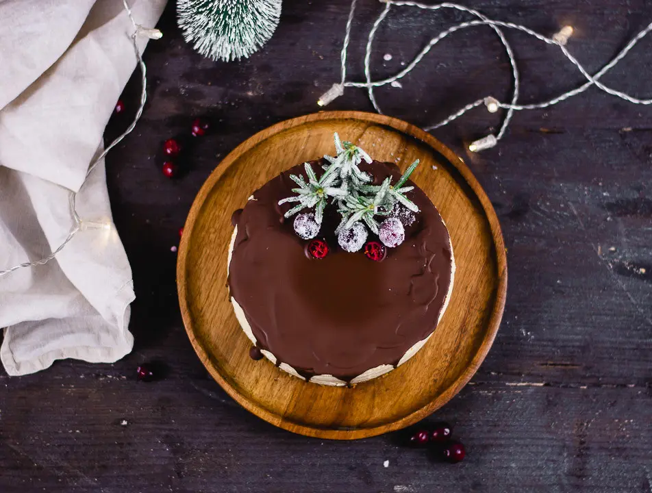 Weihnachtlicher Käsekuchen fotografiert von oben auf einem dunklen, runden Holzteller. Neben dem Teller liegt eine beige Serviette. Der Teller steht auf einer sehr dunklen Tischplatte.