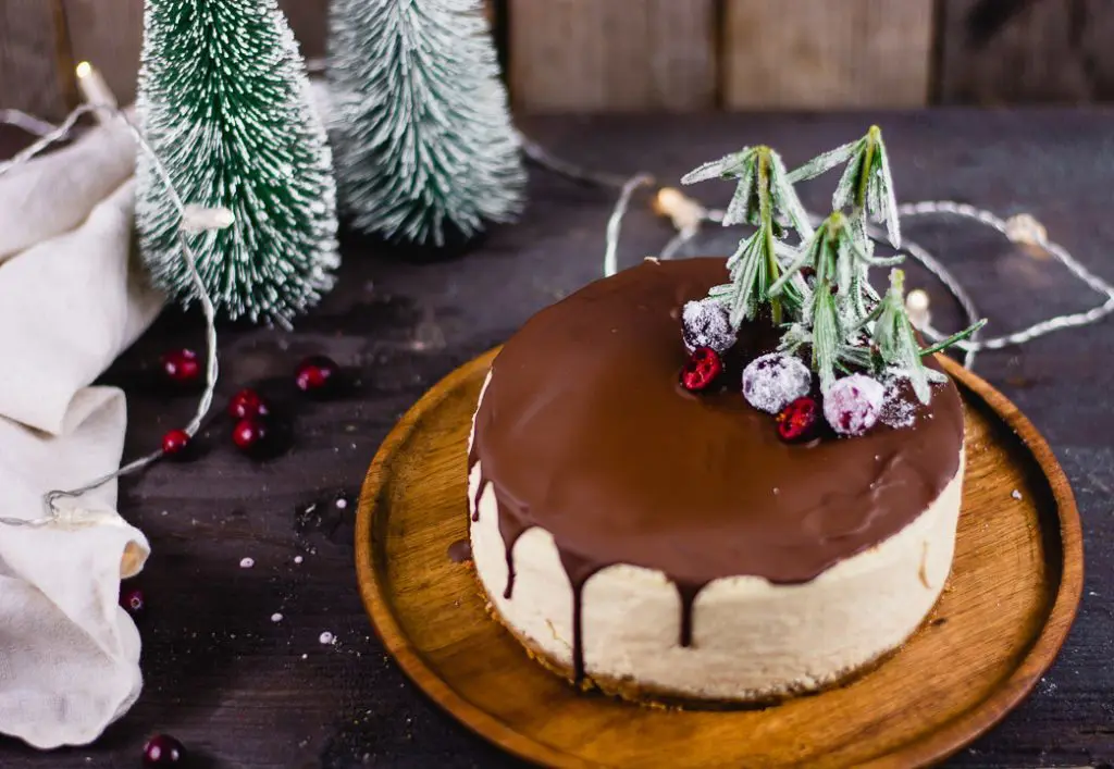 Der fertige weihnachtliche Käsekuchen auf einem runden Holzteller umgeben von weihnachtlicher Dekoration.