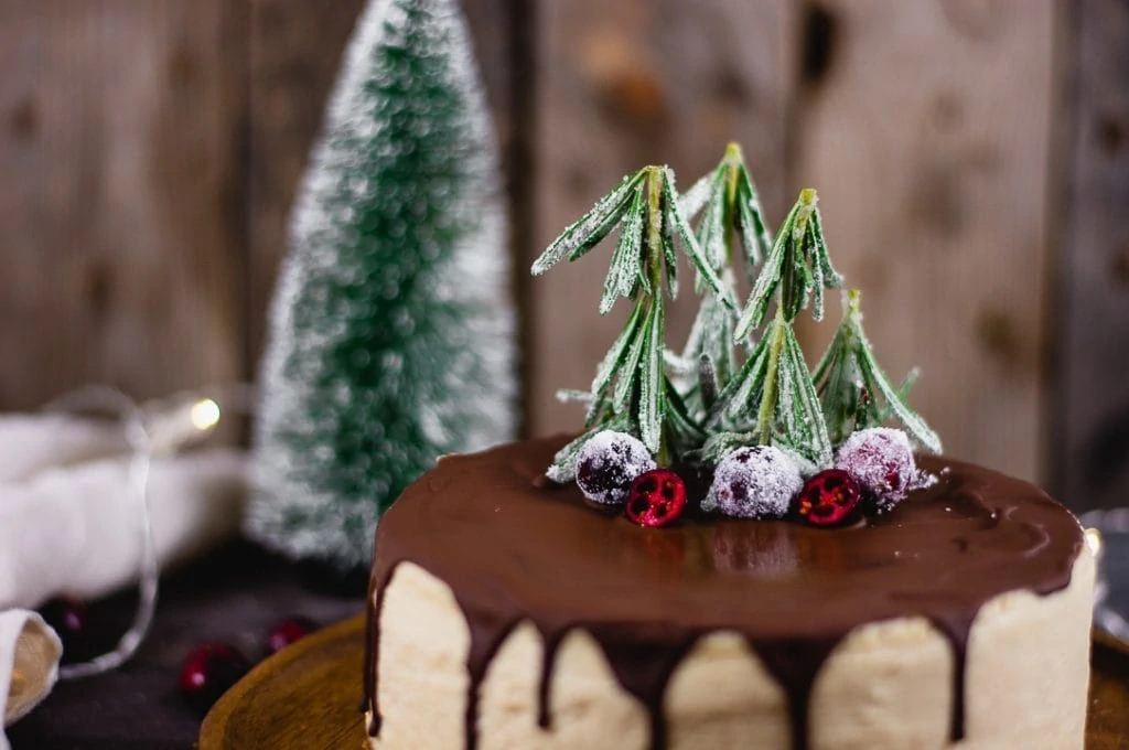 Die Dekoration des weihnachtlichen Käsekuchens besteht aus Rosmarienzweigen, die in Zucker gewälzt werden. Dadurch sehen sie aus wie kleine Tannenbäume. Außerdem liegen drei gezuckerte Cranberries auf dem Kuchen.