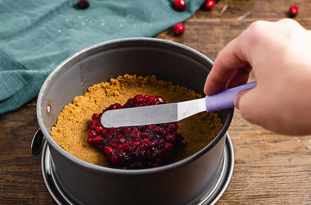 Auf dem vorgebackenen Spekulatiusboden wird mit Hilfe einer kleinen Winkelpalette Preiselbeermarmelade verteilt.