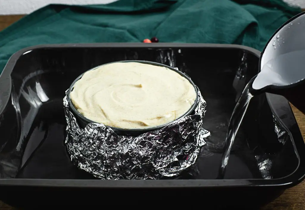 Der weihnachtliche Käsekuchen wird im Wasserbad gebacken. Dafür wird die Springform mit Alufolie ummantelt und in eine große Auflaufform gestellt. Die Auflaufform wird dann ca. 1 cm hoch mit heißem Wasser gefüllt.