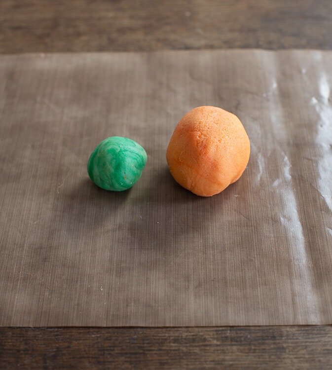 Auf einem Stück Backpapier liegen oranges und grünes Marizpan.