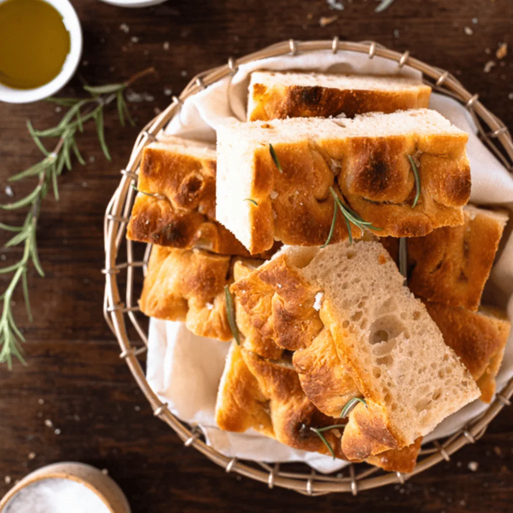 Frisch gebackenes, luftiges Focaccia Brot mit Rosmarin und grobem Salz, in Stücke geschnitten und im Korb serviert.
