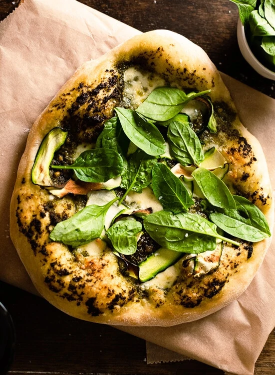 Auf der fertig gebackenen Pizza mit Pesto, Mozzarella und Zucchini kommt noch frischen Babyspinat. 