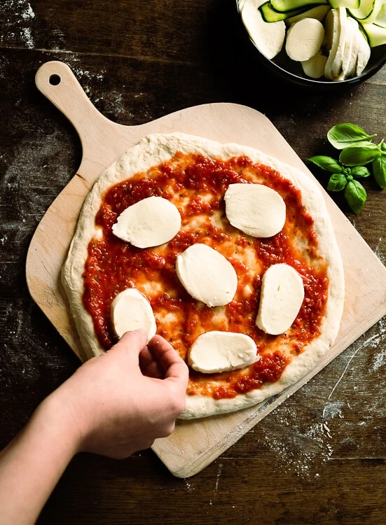 Eine Pizza wird mit Tomatensauce wird mit Mozzarella Scheiben belegt. 
