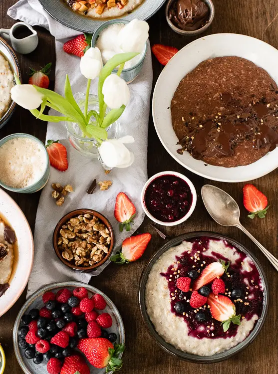 Porridge Rezepte mit Beeren Kompott und Schokolade auf gedecktem Frühstückstisch. 