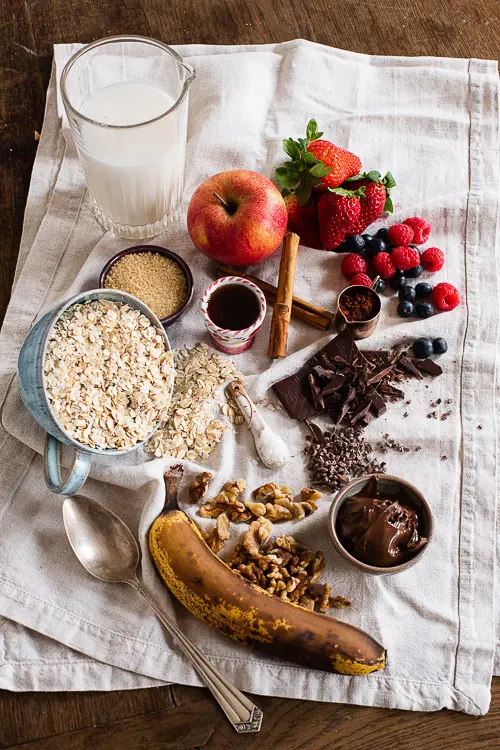 Die Zutaten für die Porridge Rezepte liegen bereit. Banane, Walnüsse, Schokocreme, Haferflocken, Apfel und Beeren gehören mit dazu.