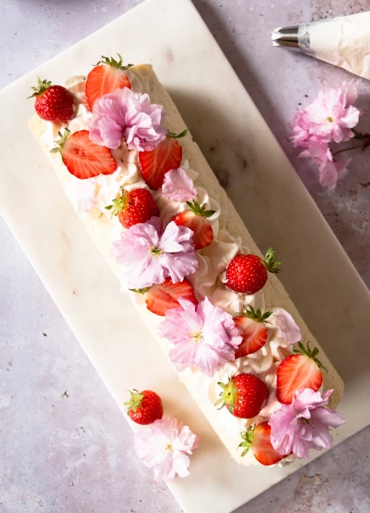 Fertig dekorierte Biskuitrolle mit Schlagsahne, frischen Erdbeeren und essbaren Blüten. 