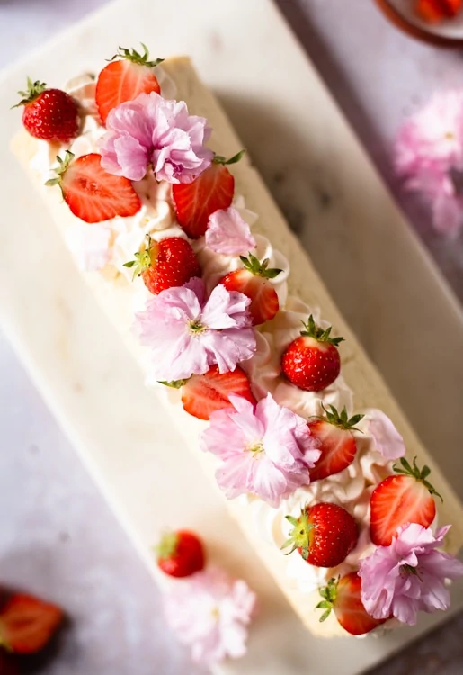 Die Biskuitrolle ist dekoriert mit geschlagener Sahne, frischen Erdbeeren und essbaren Blüten. 