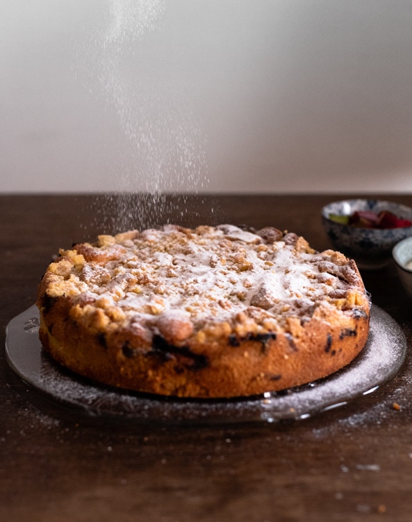 Ein Rhabarber Kuchen mit Streuseln wird mit Puderzucker bestreut.