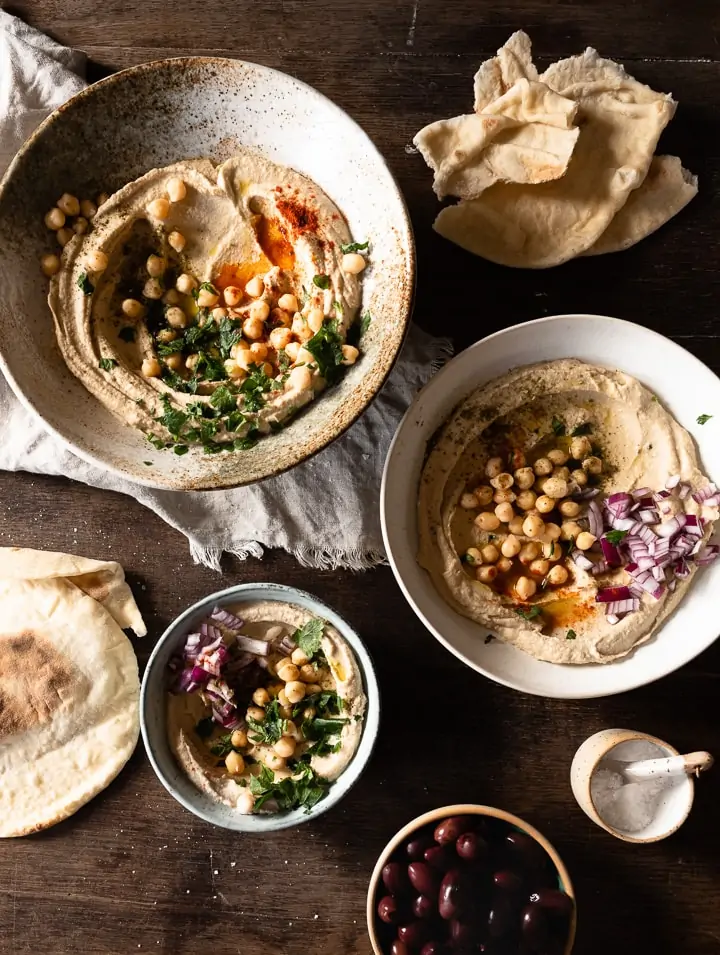 Hummus rezept original arabisch, serviert mit Olivenöl, Pitabrot und frischen Zwiebeln.