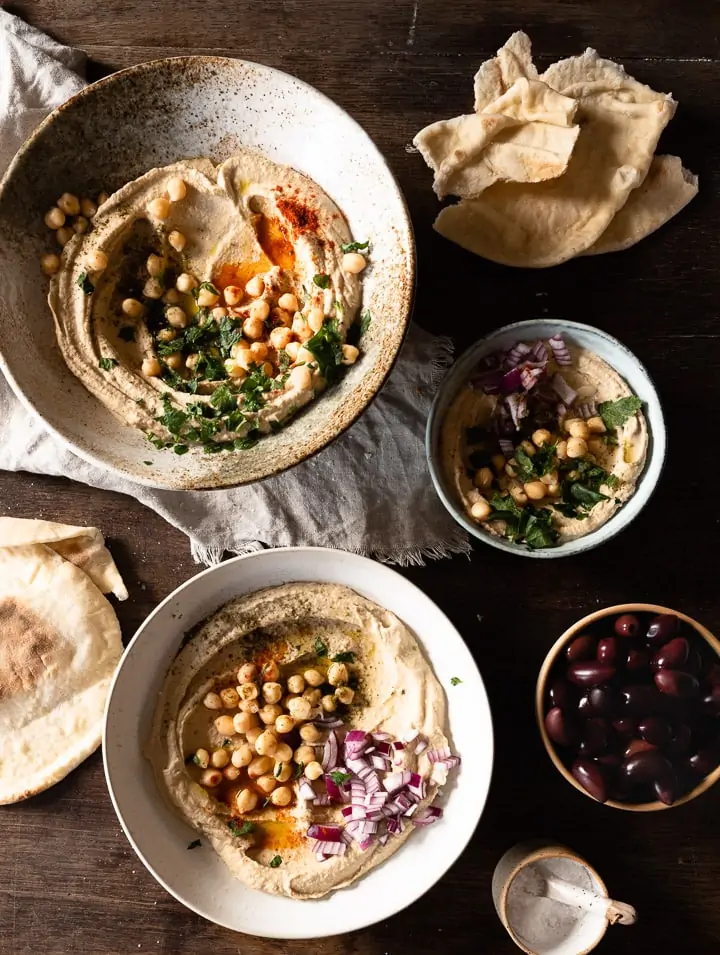 Hummus rezept original arabisch in einer Schüssel mit Oliven daneben.