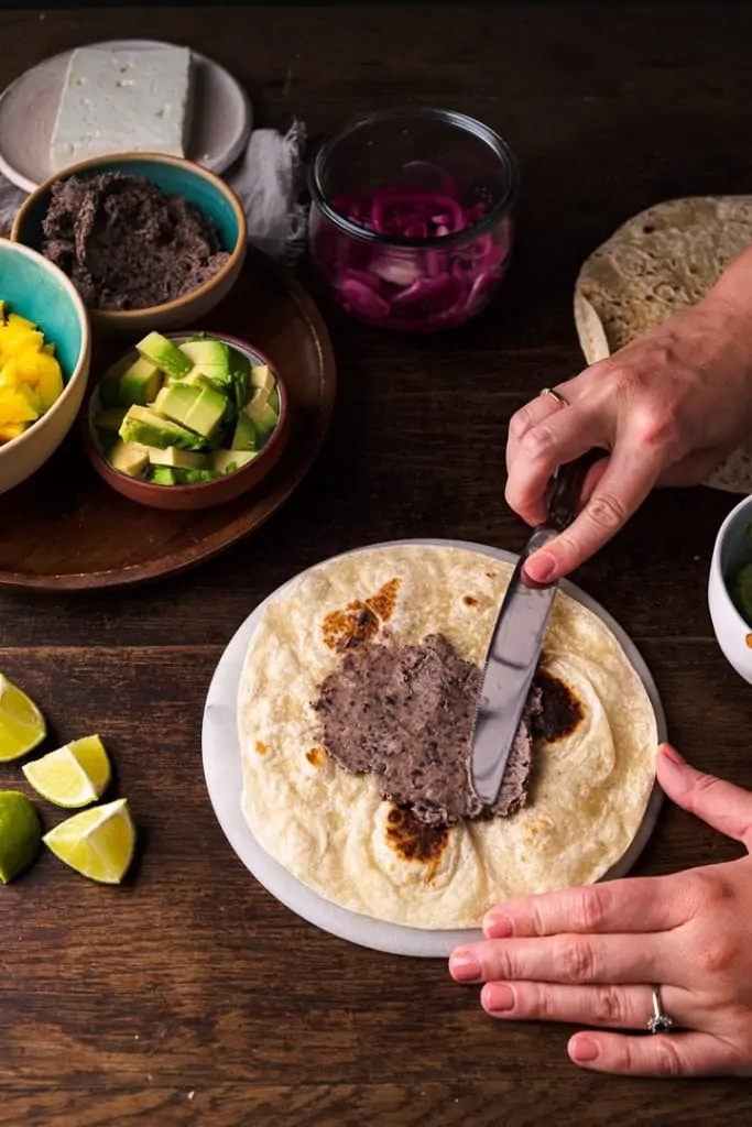 Das Bohnenmus wird auf einen Taco mit einem Messer gestrichen.