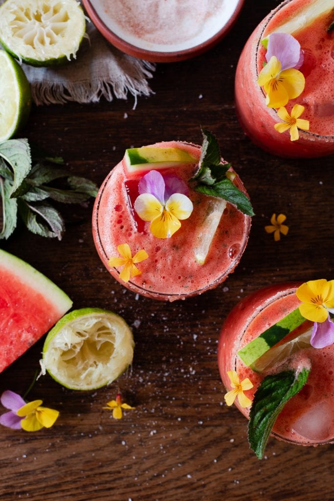 Wassermelonen Cocktail auf Eis mit Melonenspalten, Minze und essbaren Blüten serviert. 