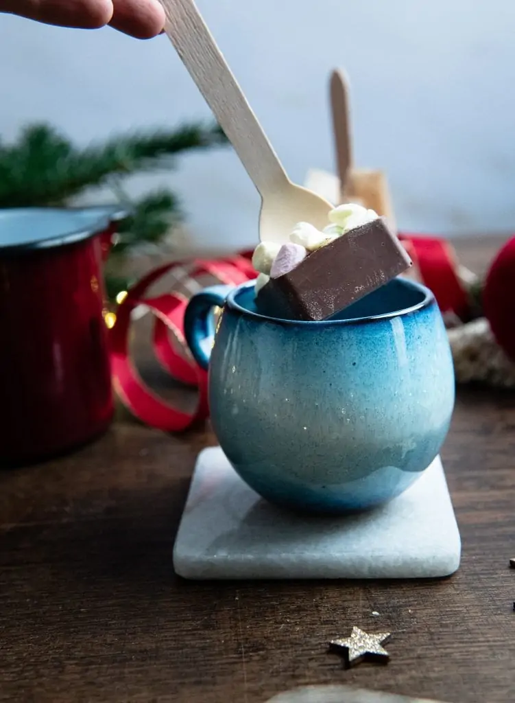 Die heiße Schokolade am Stiel wird in eine Tasse mit Milch eingetaucht.