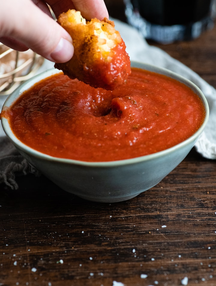 Ein Arancini wird in Tomatensauce gedippt.