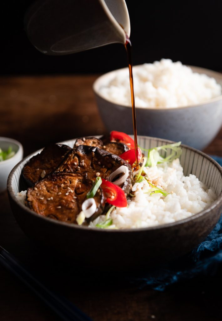 Sojasauce wird zu dem Reis und der Japanischen Aubergine in einen Teller gegossen.