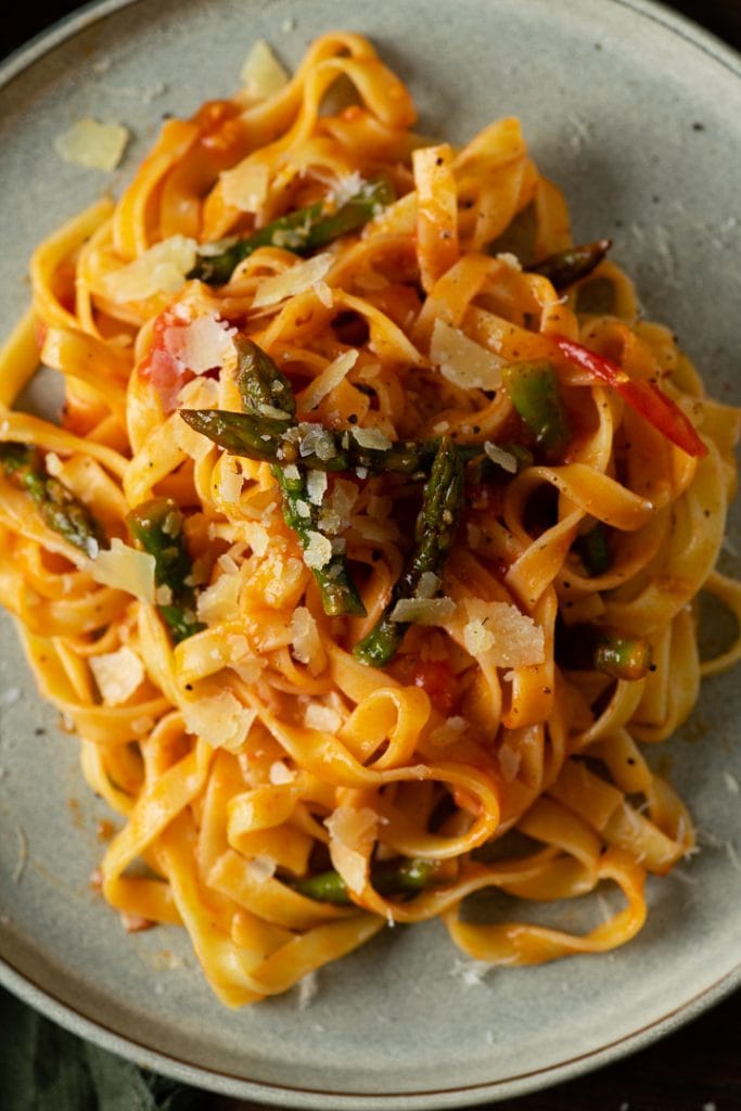 Italienische Pasta mit grünem Spargel, Tomaten und Parmesan auf dem Teller.