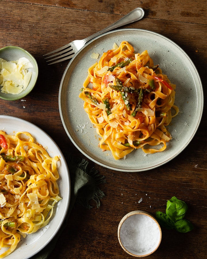 Leckere Pasta mit grünem Spargel, Tomaten und Parmesan auf einem Teller.