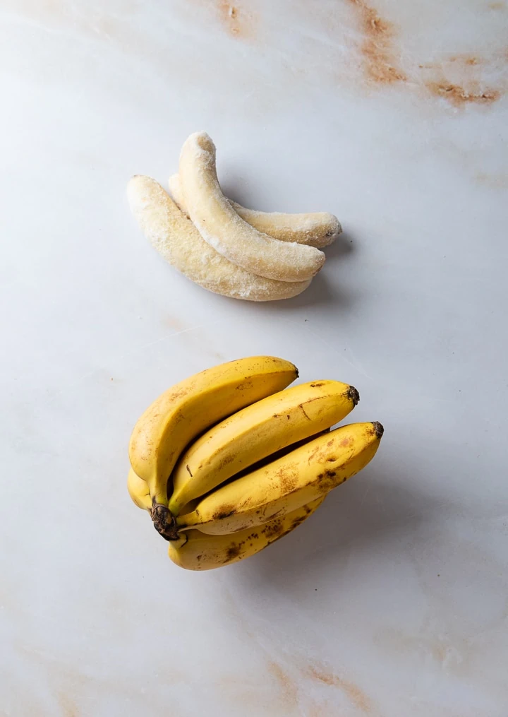 Einmal frische Bananen und einmal eingefrorene Bananen liegen auf dem Tisch.