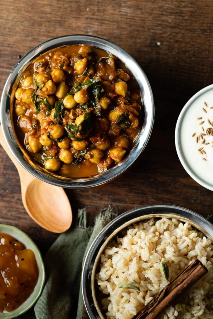 Auf einem Tisch steht das vegane Kichererbsen Spinat Curry mit einer Schale Reis.
